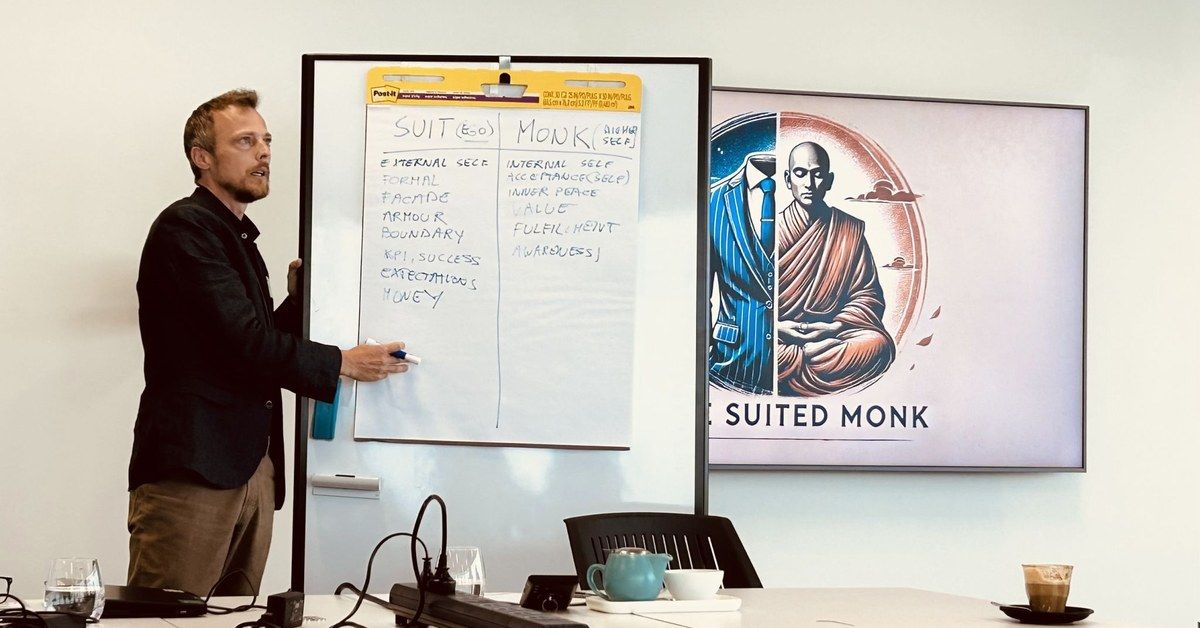 Raf Adams presenting a Suit and Monk flipchart, outer self versus inner self, beside a Suited Monk screen in a workshop