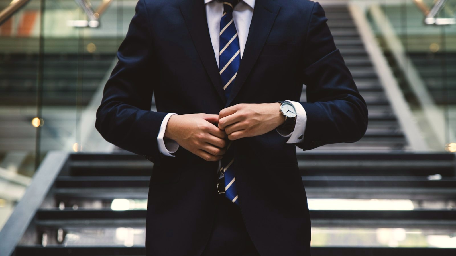 A professional in a navy suit adjusting his jacket in a corporate lobby, outwardly successful yet personally anonymous — a picture of feeling stuck in a career despite success.